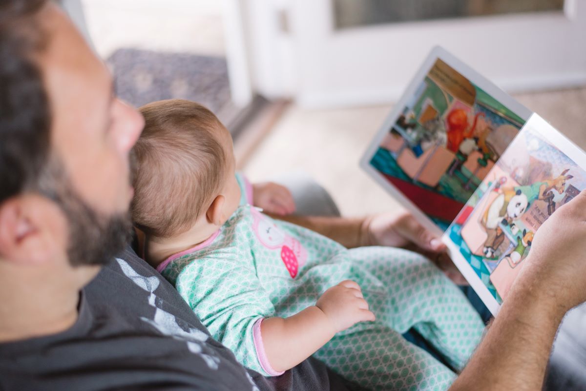 Man with a baby in his lap, reading a children's book during custody hours.