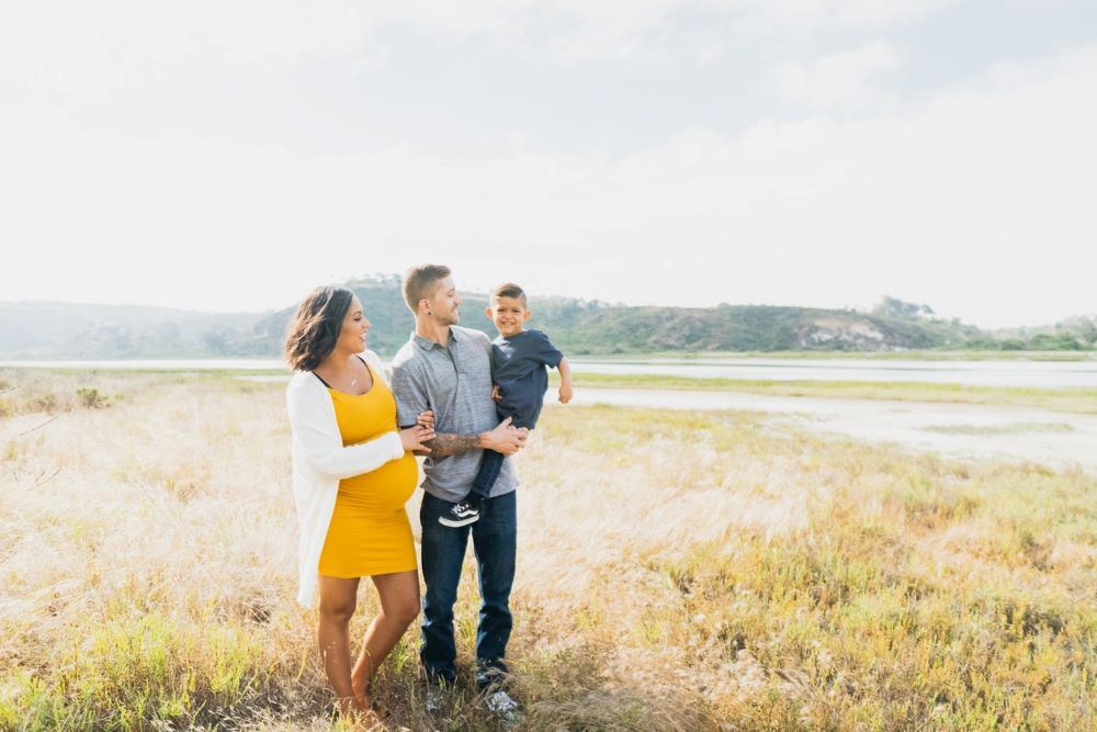 A pregnant woman and a man holding a young boy standing outside.